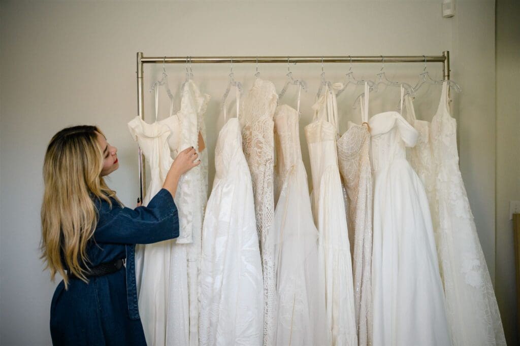 Seamstress examining a wedding dress on a rack in a bridal studio.