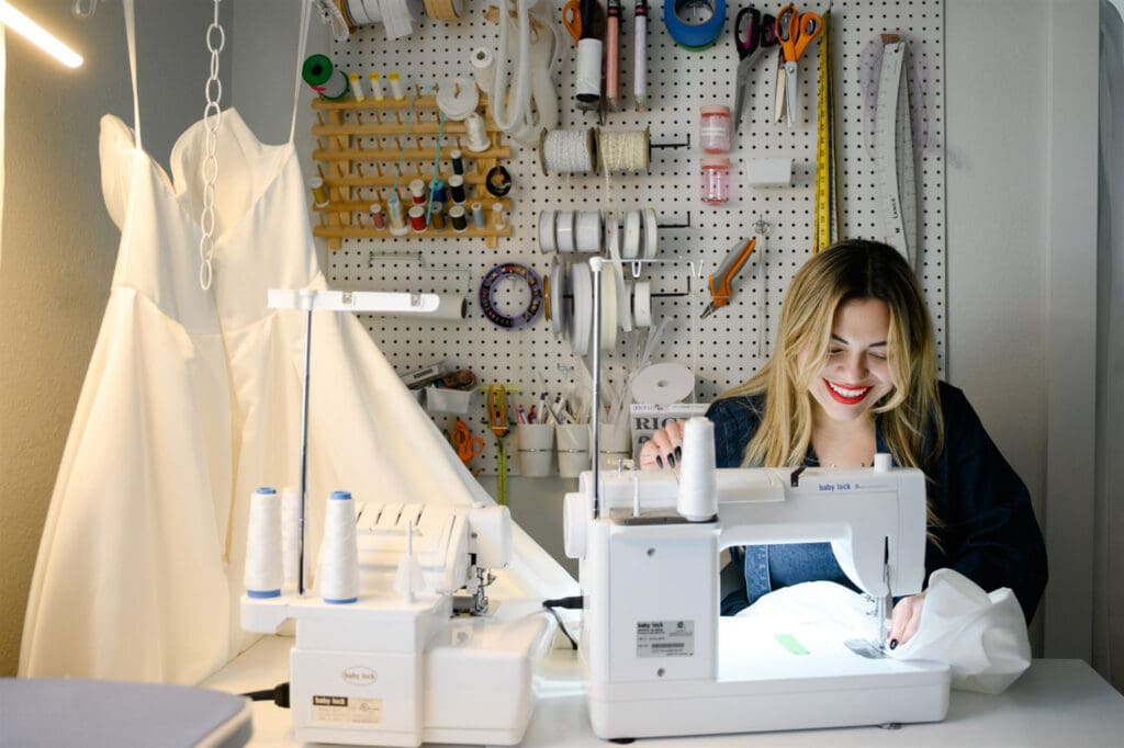 Seamstress sewing a wedding dress at a sewing machine in a bridal alterations studio.