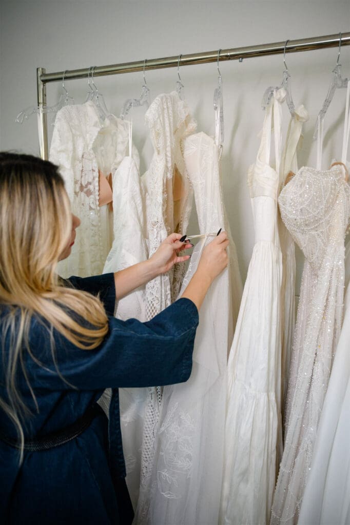 Seamstress examining a wedding dress on a rack in a bridal studio.