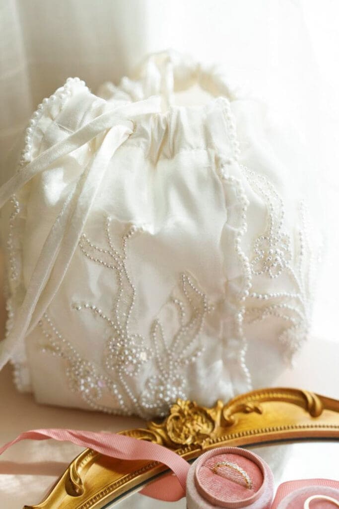 Beaded bridal drawstring bag with wedding rings in pink ring box.