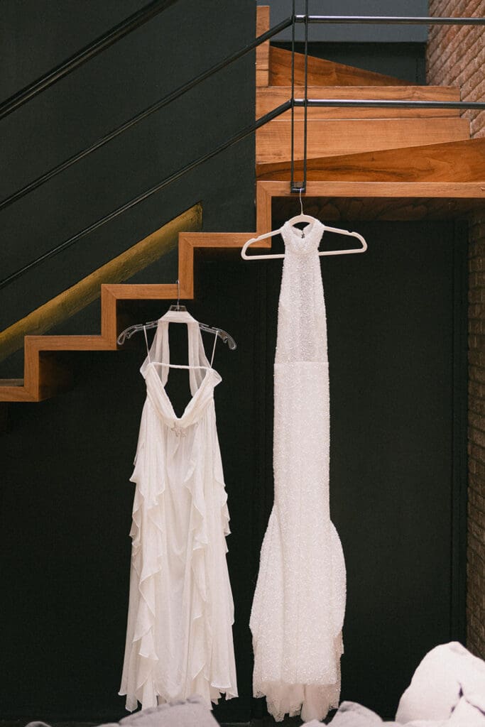 Two wedding dresses hanging on hangers beneath a modern staircase.
