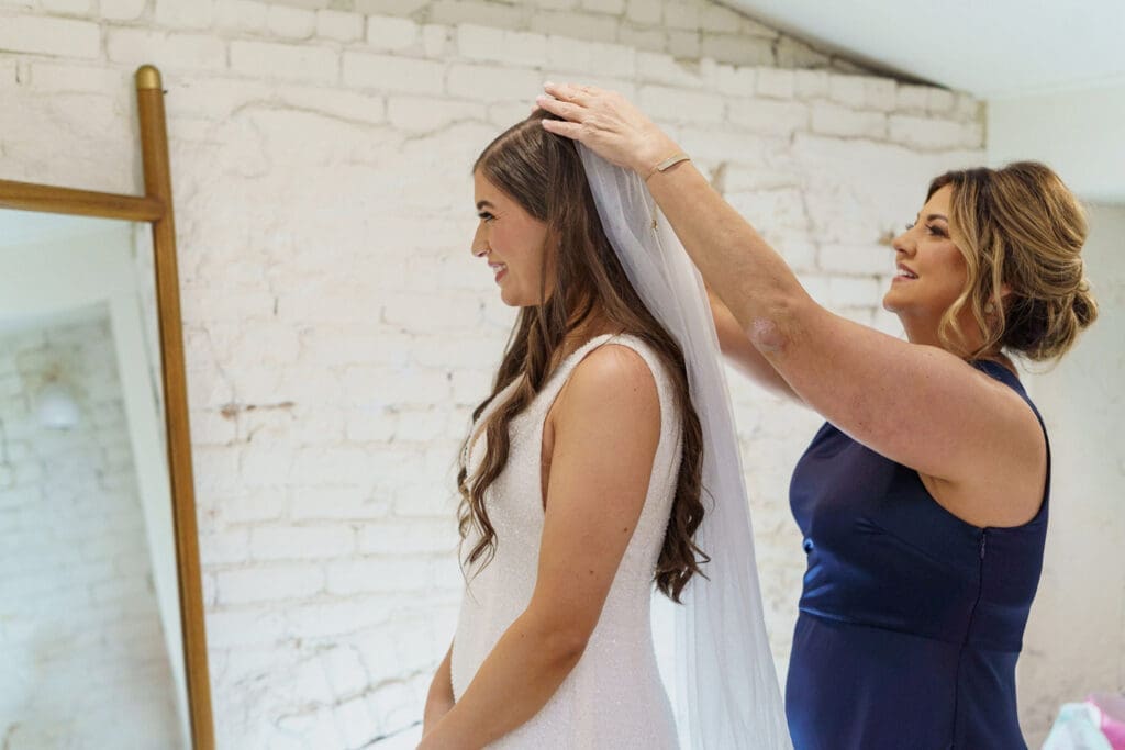 Woman adjusting a bride’s veil during wedding dress fitting.