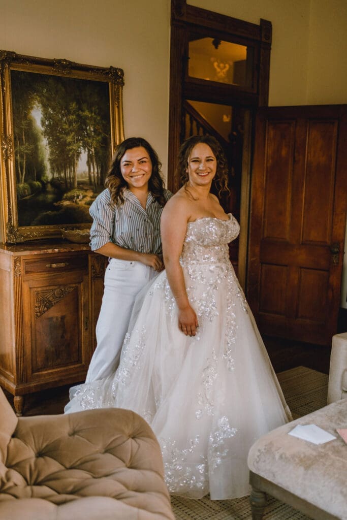 Bride smiling while seamstress adjusts her wedding gown during fitting.